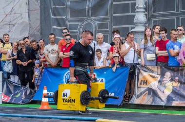 Lviv, Ukrayna - Ağustos 2017: Güçlü atlet bir vücut geliştirmeci egzersiz ağır demir bavul bir çiftçinin yürüyüş, coşkulu seyirci önünde strongmen oyun taşır