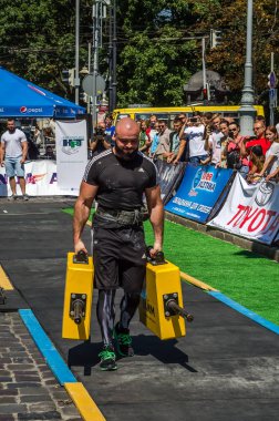 Lviv, Ukrayna - Ağustos 2017: Güçlü atlet bir vücut geliştirmeci egzersiz ağır demir bavul bir çiftçinin yürüyüş, coşkulu seyirci önünde strongmen oyun taşır