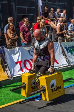 Lviv, Ukrayna - Ağustos 2017: Güçlü atlet bir vücut geliştirmeci egzersiz ağır demir bavul bir çiftçinin yürüyüş, coşkulu seyirci önünde strongmen oyun taşır