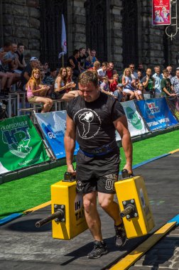 Lviv, Ukrayna - Ağustos 2017: Güçlü atlet bir vücut geliştirmeci egzersiz ağır demir bavul bir çiftçinin yürüyüş, coşkulu seyirci önünde strongmen oyun taşır