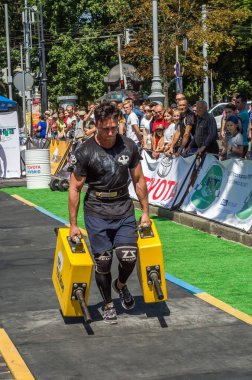 Lviv, Ukrayna - Ağustos 2017: Güçlü atlet bir vücut geliştirmeci egzersiz ağır demir bavul bir çiftçinin yürüyüş, coşkulu seyirci önünde strongmen oyun taşır