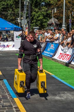 Lviv, Ukrayna - Ağustos 2017: Güçlü atlet bir vücut geliştirmeci egzersiz ağır demir bavul bir çiftçinin yürüyüş, coşkulu seyirci önünde strongmen oyun taşır