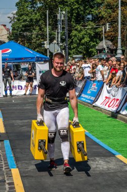 Lviv, Ukrayna - Ağustos 2017: Güçlü atlet bir vücut geliştirmeci egzersiz ağır demir bavul bir çiftçinin yürüyüş, coşkulu seyirci önünde strongmen oyun taşır