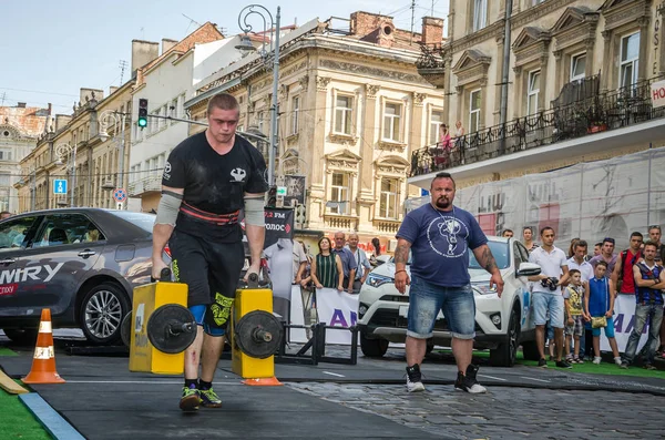 LVIV, UCRANIA - AGOSTO 2017: Un atleta fuerte un culturista lleva maletas pesadas de hierro, en el ejercicio de un paseo del agricultor, en el juego de los hombres fuertes en frente de espectadores entusiastas — Foto de Stock