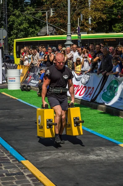 LVIV, UCRANIA - AGOSTO 2017: Un atleta fuerte un culturista lleva maletas pesadas de hierro, en el ejercicio de un paseo del agricultor, en el juego de los hombres fuertes en frente de espectadores entusiastas — Foto de Stock