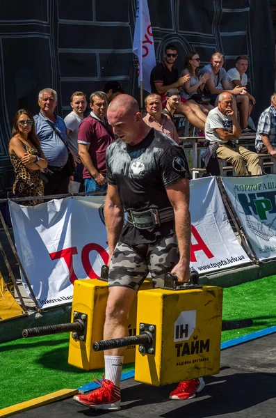 LVIV, UCRANIA - AGOSTO 2017: Un atleta fuerte un culturista lleva maletas pesadas de hierro, en el ejercicio de un paseo del agricultor, en el juego de los hombres fuertes en frente de espectadores entusiastas — Foto de Stock