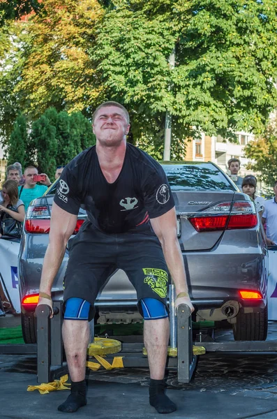 LVIV, UCRANIA - AGOSTO 2017: Fuerte atleta el culturista levanta el coche Toyota frente a los espectadores entusiastas en el juego Strongmen — Foto de Stock