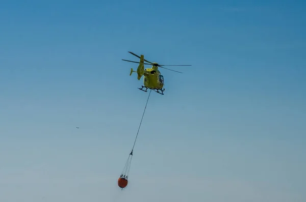 Roma, Włochy - lipca 2017: Helikopter strażacki jest podniesienie wody w koszyku do gaszenia pożaru na Morzu Tyrreńskim w pobliżu Ostia, Włochy — Zdjęcie stockowe