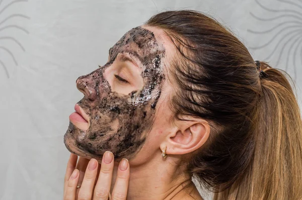 युवा आकर्षक मुलगी करते एक ब्लॅक कोळसा मुखवटा तिच्या चेहरा — स्टॉक फोटो, इमेज