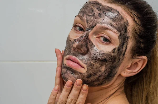 Joven chica encantadora hace una máscara de carbón negro en su cara — Foto de Stock