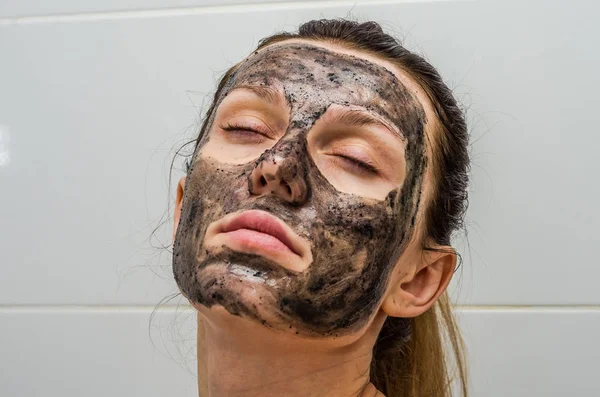Joven chica encantadora hace una máscara de carbón negro en su cara — Foto de Stock