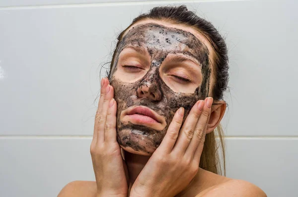 Menina encantadora jovem faz uma máscara de carvão preto em seu rosto — Fotografia de Stock