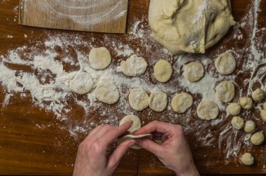 Bir kadın aşçı el un hamur bir tablo üzerinde pişmiş ve vareniki yapmak