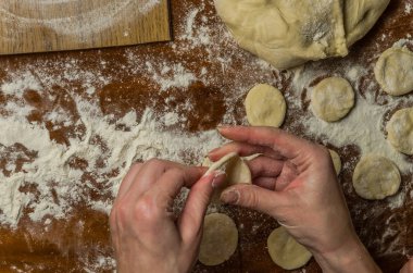 Bir kadın aşçı el un hamur bir tablo üzerinde pişmiş ve vareniki yapmak