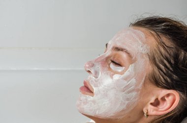 Genç güzel kız banyoda spa uygulamaları sırasında beyaz yüz maskesi güzellik için yapar