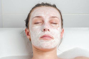 Genç güzel kız banyoda spa uygulamaları sırasında beyaz yüz maskesi güzellik için yapar