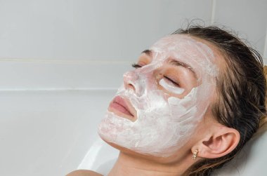Genç güzel kız banyoda spa uygulamaları sırasında beyaz yüz maskesi güzellik için yapar