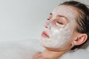 Genç güzel kız banyoda spa uygulamaları sırasında beyaz yüz maskesi güzellik için yapar