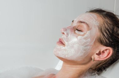Genç güzel kız banyoda spa uygulamaları sırasında beyaz yüz maskesi güzellik için yapar
