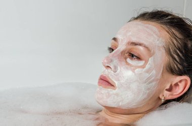 Genç güzel kız banyoda spa uygulamaları sırasında beyaz yüz maskesi güzellik için yapar