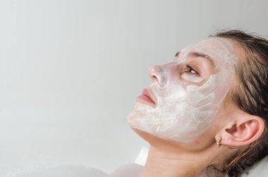 Genç güzel kız banyoda spa uygulamaları sırasında beyaz yüz maskesi güzellik için yapar