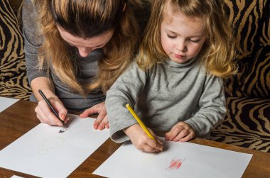 Genç güzel anne kızıyla birlikte çizmek ile renkli kalemler kağıt üzerinde mutlu bir aile