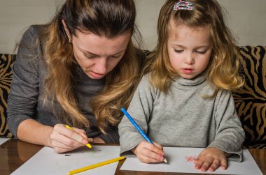 Genç güzel anne kızıyla birlikte çizmek ile renkli kalemler kağıt üzerinde mutlu bir aile
