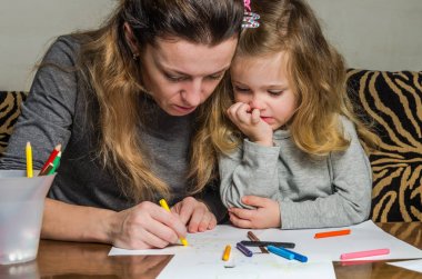 Genç güzel anne kızıyla birlikte çizmek ile renkli kalemler kağıt üzerinde mutlu bir aile