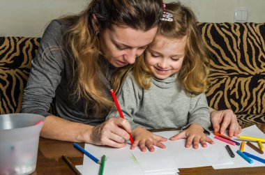 Genç güzel anne kızıyla birlikte çizmek ile renkli kalemler kağıt üzerinde mutlu bir aile