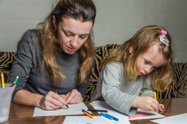 Genç güzel anne kızıyla birlikte çizmek ile renkli kalemler kağıt üzerinde mutlu bir aile