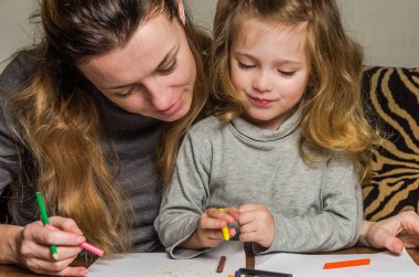 Genç güzel anne kızıyla birlikte çizmek ile renkli kalemler kağıt üzerinde mutlu bir aile
