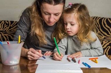 Genç güzel anne kızıyla birlikte çizmek ile renkli kalemler kağıt üzerinde mutlu bir aile