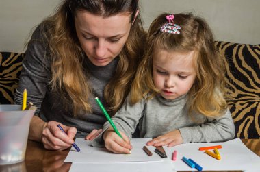Genç güzel anne kızıyla birlikte çizmek ile renkli kalemler kağıt üzerinde mutlu bir aile