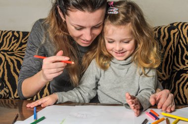 Genç güzel anne kızıyla birlikte çizmek ile renkli kalemler kağıt üzerinde mutlu bir aile