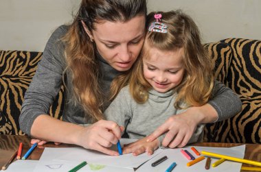 Genç güzel anne kızıyla birlikte çizmek ile renkli kalemler kağıt üzerinde mutlu bir aile