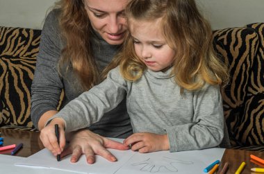 Genç güzel anne kızıyla birlikte çizmek ile renkli kalemler kağıt üzerinde mutlu bir aile