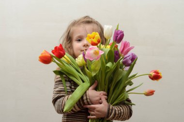 Mutlu bebek kız sevinir ve çok renkli Lale elinde bir buket gülümser