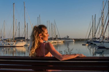 Limandaki bankta oturan genç bir kız lüks yatların arasında.