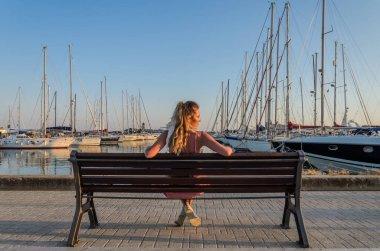 Limandaki bankta oturan genç bir kız lüks yatların arasında.