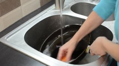 Bir kadın bulaşık deterjanıyla lavaboda bulaşık yıkıyor.