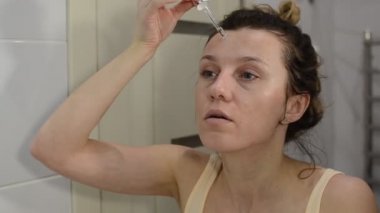 Genç ve güzel bir kız, yüzünde bir pipetle kozmetik serumu sürüyor.