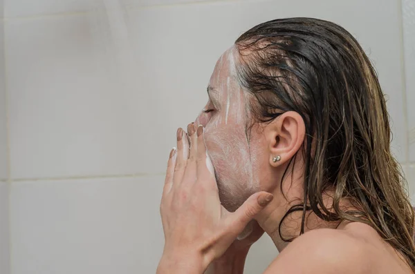 年轻迷人的性感女孩在浴室的脸上做了一个白色的洗涤剂面具 — 图库照片