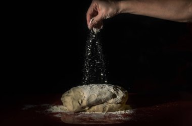 Şef, siyah arka planda beyaz un serpiştiriyor.