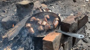 Bir adam piknikte ormanda ateşte ızgara sosis kızartıyor.