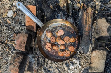 Kızarmış sosisler, piknikteki bir yangında tavada kızartılır.
