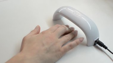 Kadın morötesi lambanın altında jel oje kurutuyor.