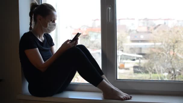 Una Chica Joven Con Una Máscara Médica Sienta Alféizar Ventana — Vídeos de Stock