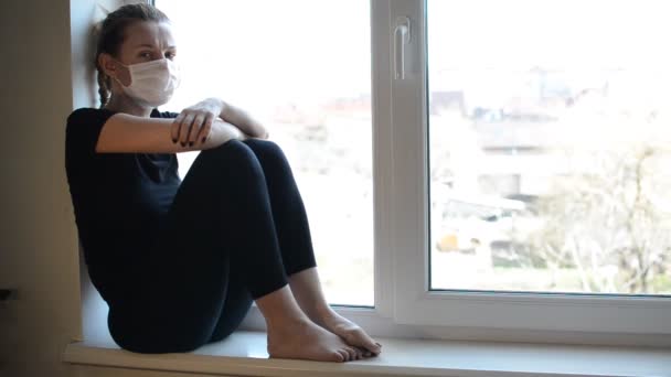 戴着口罩的小女孩坐在靠近窗户的窗台上 — 图库视频影像