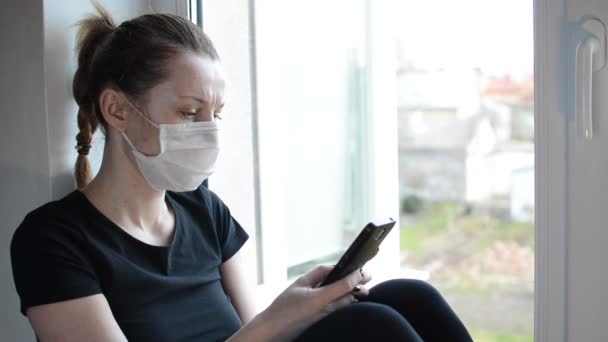 Una Chica Joven Con Una Máscara Médica Sienta Alféizar Ventana — Vídeos de Stock