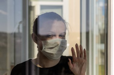 Tıbbi maske takan genç kız pencerede duruyor.